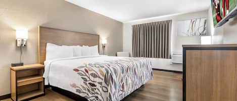 A hotel room with a large bed, a desk, a flat-screen TV, and a window with curtains.