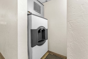 A compact, white, wall-mounted water dispenser with a Scotsman logo, located in a corner of a room with textured walls and a wooden floor. - Red Roof Inn Huntsville, AL (Huntsville)