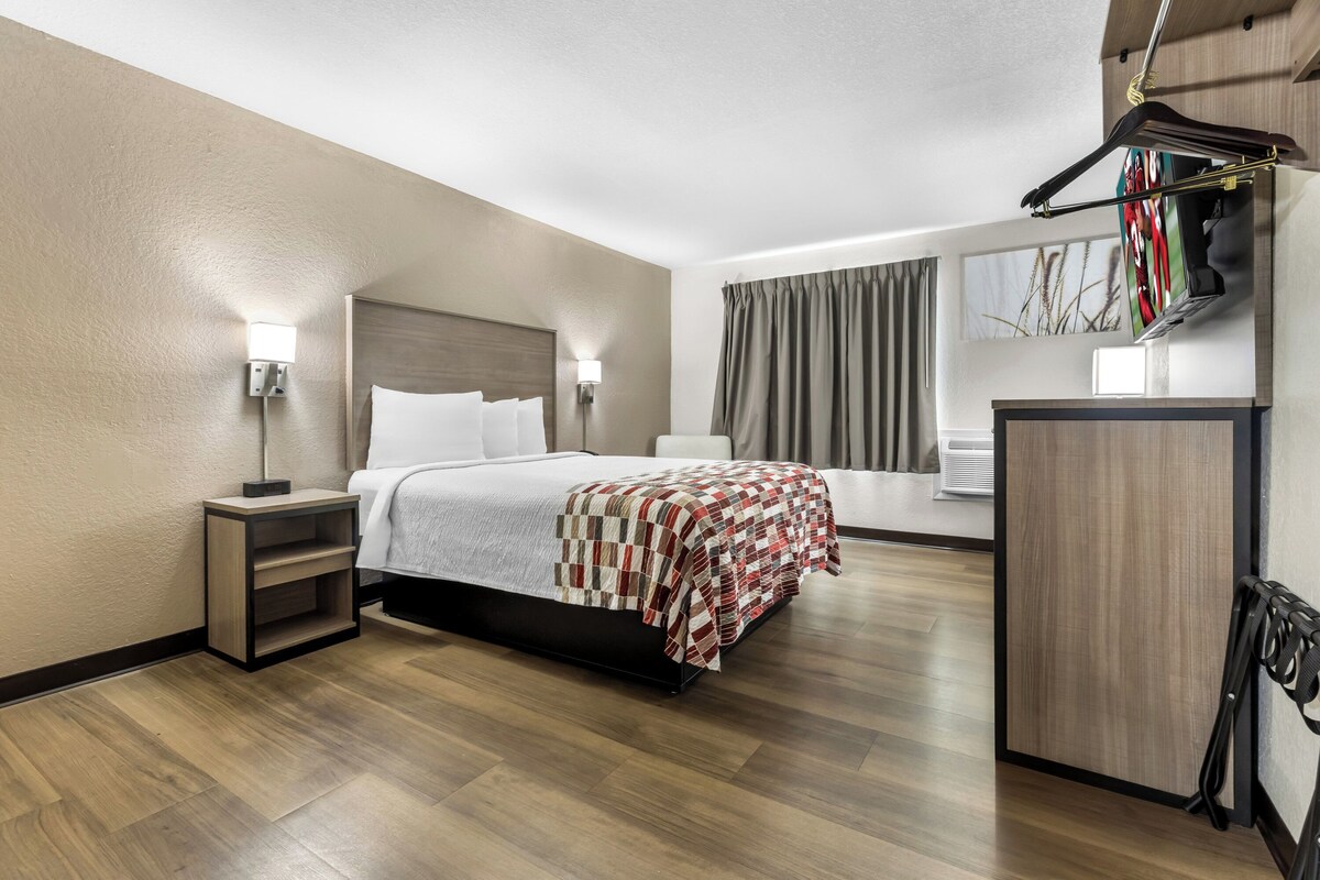 Habitación de hotel con cama, mesitas de noche, armario, espejo y ventana con cortinas.