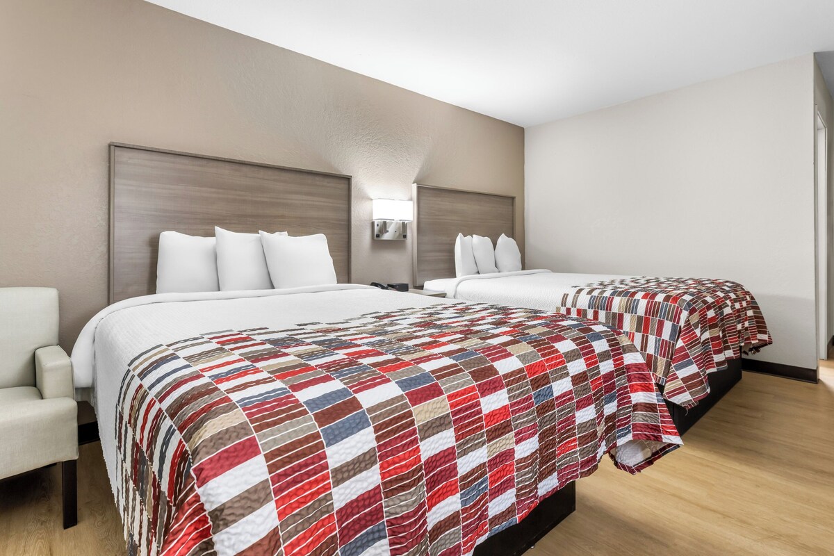 Una habitación de hotel con dos camas, una mesita de noche y una silla.