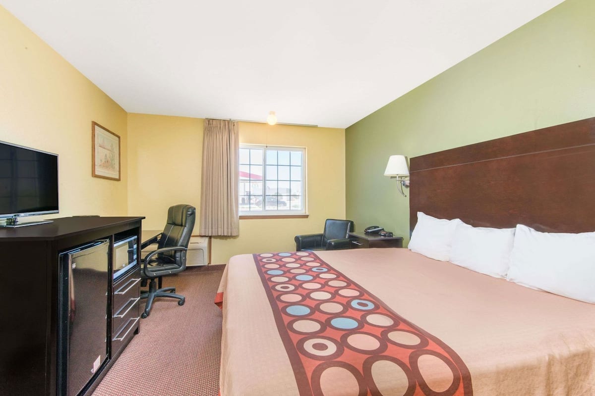 Quarto de hotel com cama, escrivaninha com cadeira, televisão e janela.