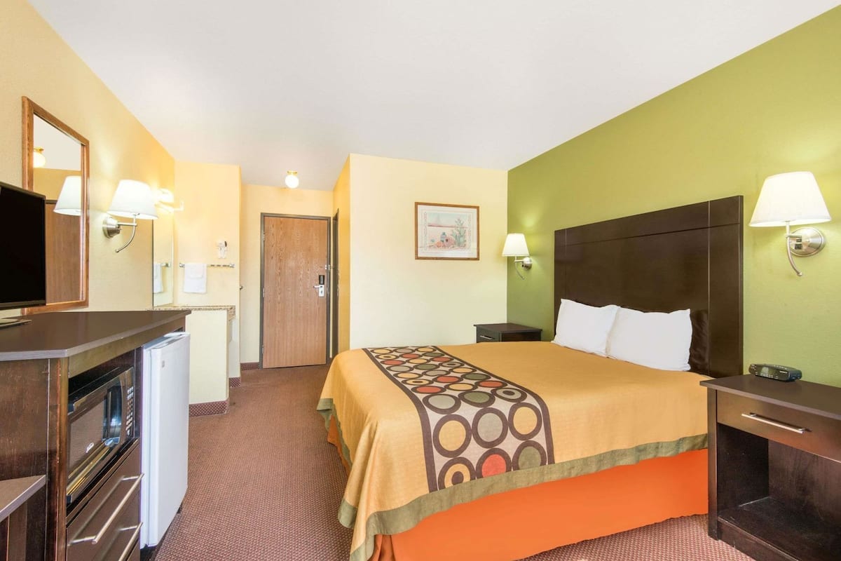 Quarto de hotel com uma cama, uma escrivaninha com televisão, um pequeno frigorífico e uma porta que dá para outro quarto.