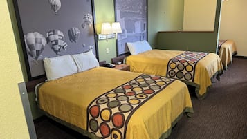 Una habitación de hotel con dos camas, cada una con una colcha estampada, una mesita de noche con lámpara y una pared decorada con un cuadro de globos aerostáticos.