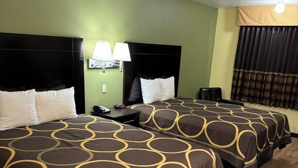 A hotel room with two beds, each with a brown and yellow patterned bedspread, a black headboard, a nightstand with a lamp, and a wooden floor. - Super 8 by Wyndham Moriarty (Moriarty)