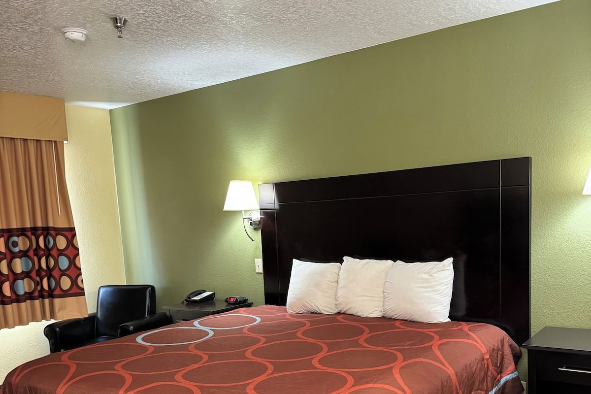 Quarto de hotel com uma cama grande, mesa de cabeceira, luminária e uma cadeira.