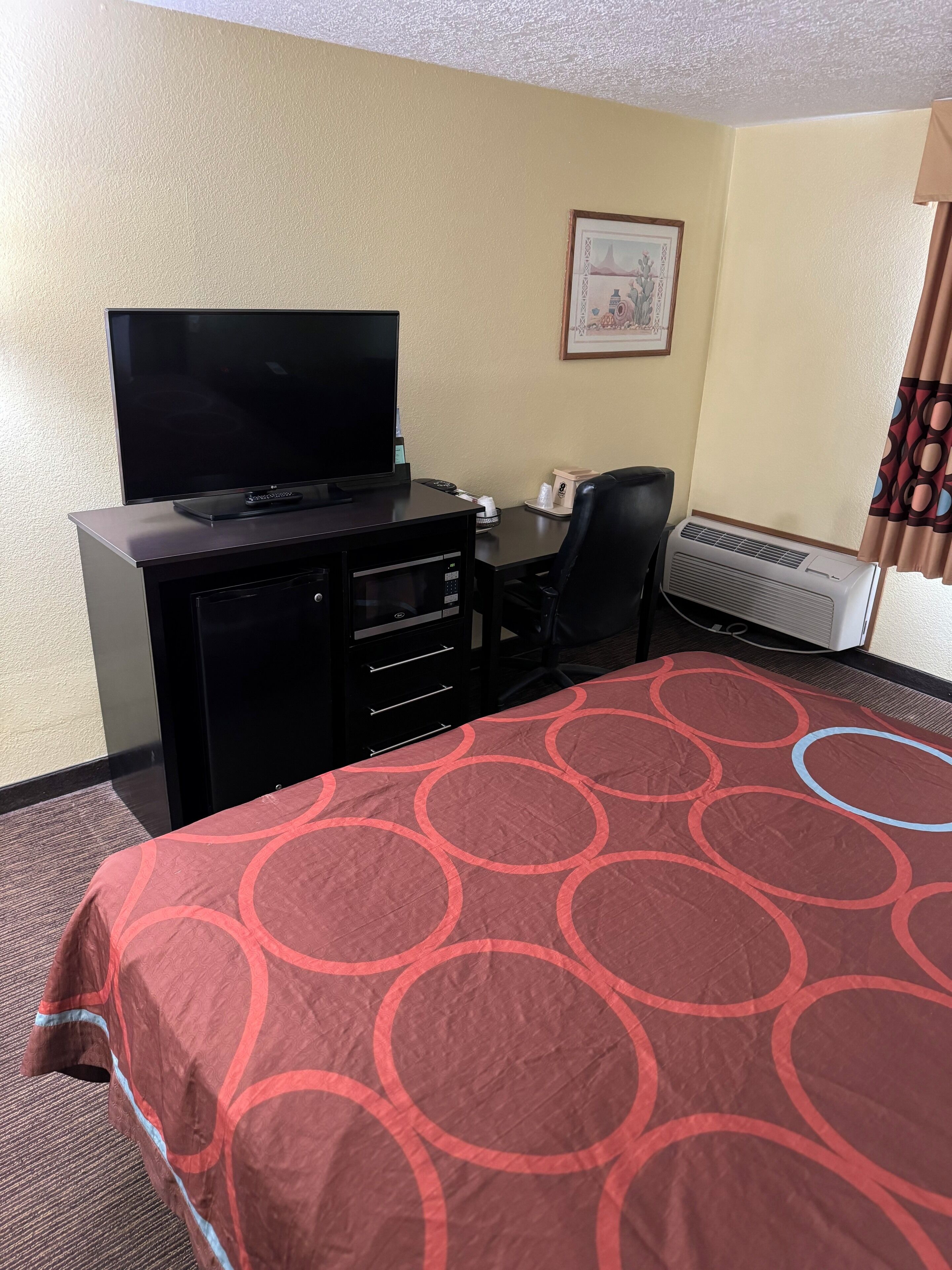 Habitación de hotel con cama, escritorio con ordenador, televisor y aire acondicionado.