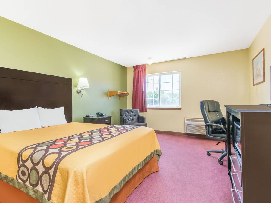 Una habitación de hotel con cama, escritorio, silla, lámpara y ventana.