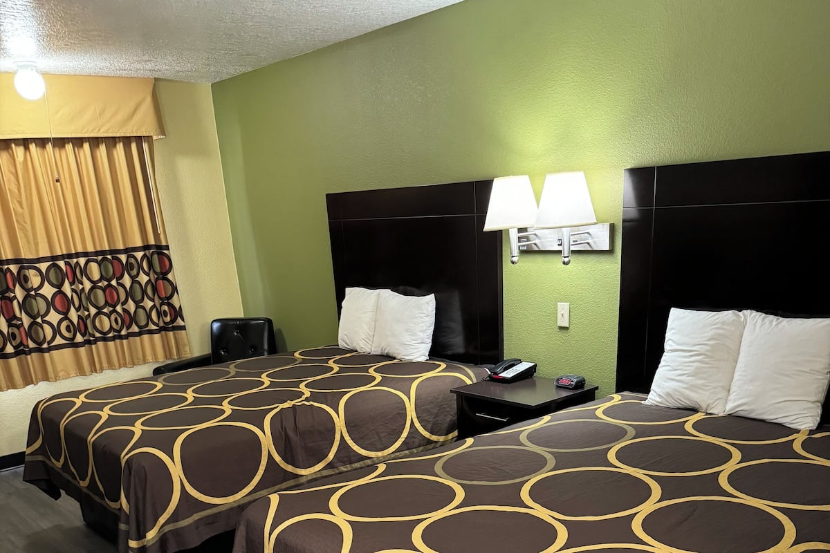 Quarto de hotel com duas camas, cada uma com colcha marrom e amarela estampada, cabeceira preta e mesa de cabeceira com abajur.