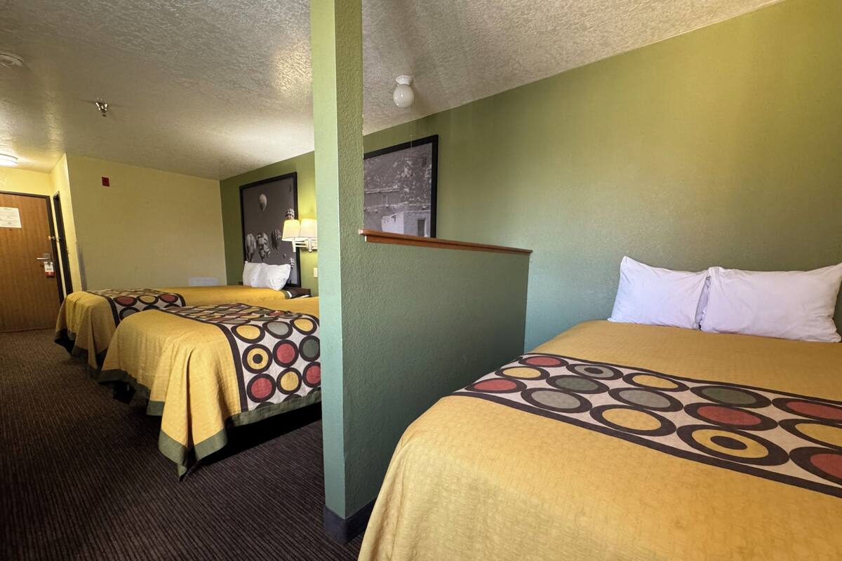 Quarto de hotel com três camas de solteiro, cada uma com colcha estampada.