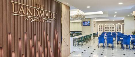 Un interior moderno con una pared de madera que muestra el letrero "The Landmark A Gathering Place", una araña y una zona de comedor con sillas y mesas azules.