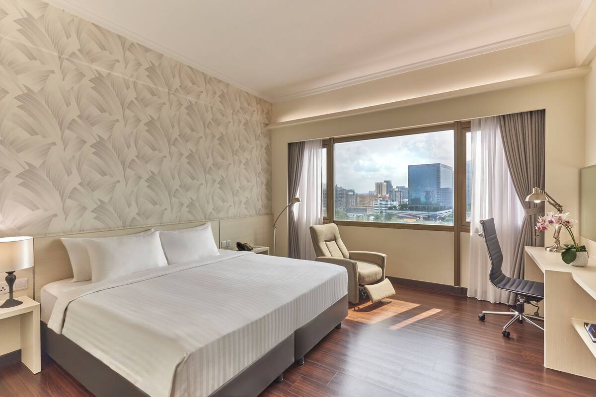 Habitación de hotel con una cama grande, un escritorio, una silla y vista a la ciudad.