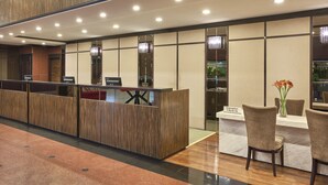 Una recepción con diseño moderno, un mostrador de check-in y una zona de espera con sillas y una mesa.
