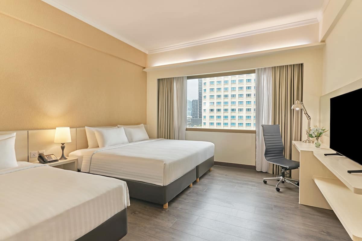 Habitación de hotel con dos camas, un escritorio, una silla, un televisor y una ventana con vistas a la ciudad.