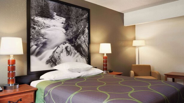 A hotel room with a bed, two bedside tables, a chair, a desk, and a large framed picture on the wall.