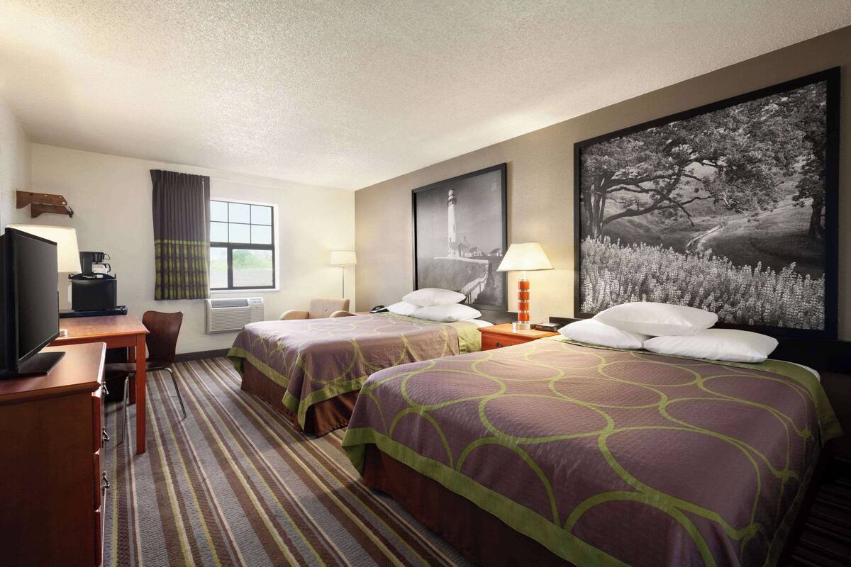 Een hotelkamer met twee bedden, een bureau met een televisie, een stoel, een raam met gordijnen en een schilderij aan de muur.