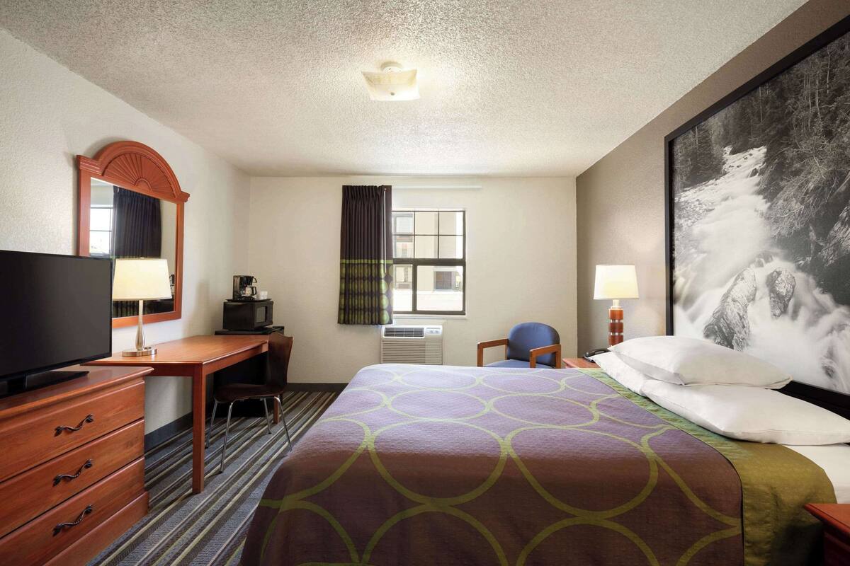 Een hotelkamer met een bed, een bureau, een televisie, een stoel, een groot raam en een schilderij aan de muur.