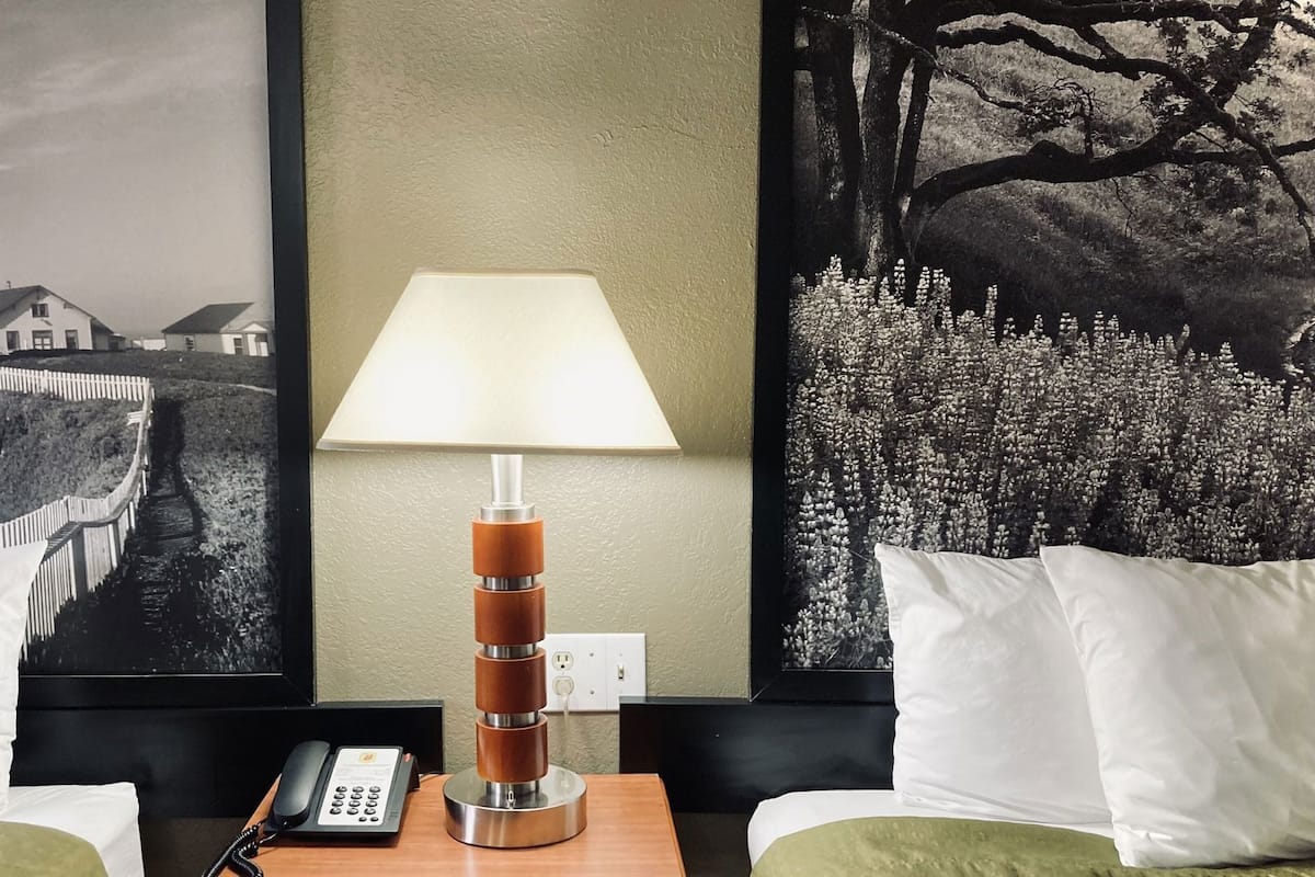 Een hotelkamer met een bed, nachtkastje met lamp, telefoon en twee kussens.