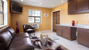 A modern kitchen with a glass-top table, brown leather sofa, and a red vase.