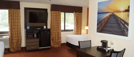 Habitación de hotel con cama, escritorio, silla, televisor, microondas y cafetera.