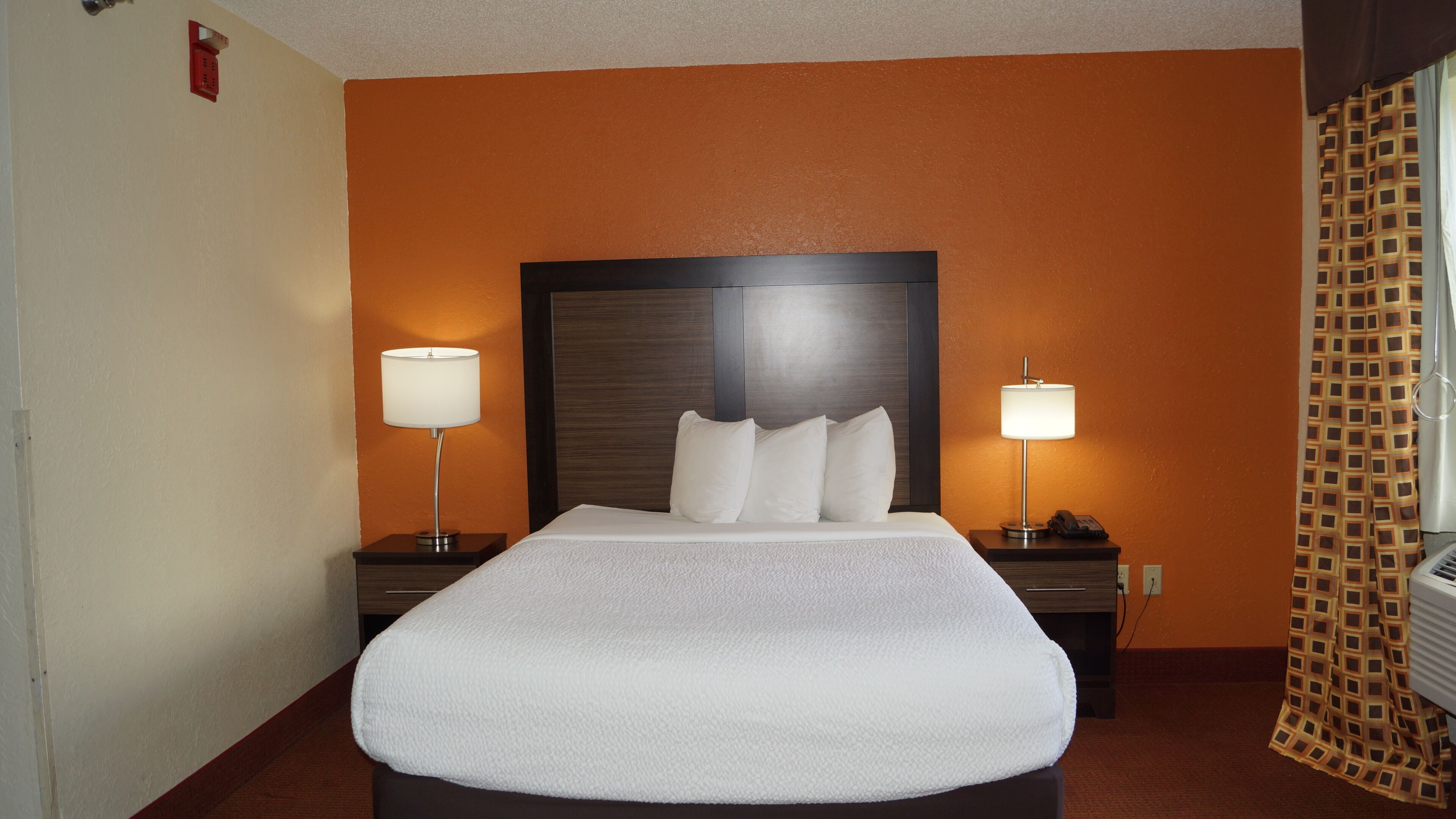 A hotel room with a large bed, two bedside tables with lamps, a telephone, and a patterned curtain.