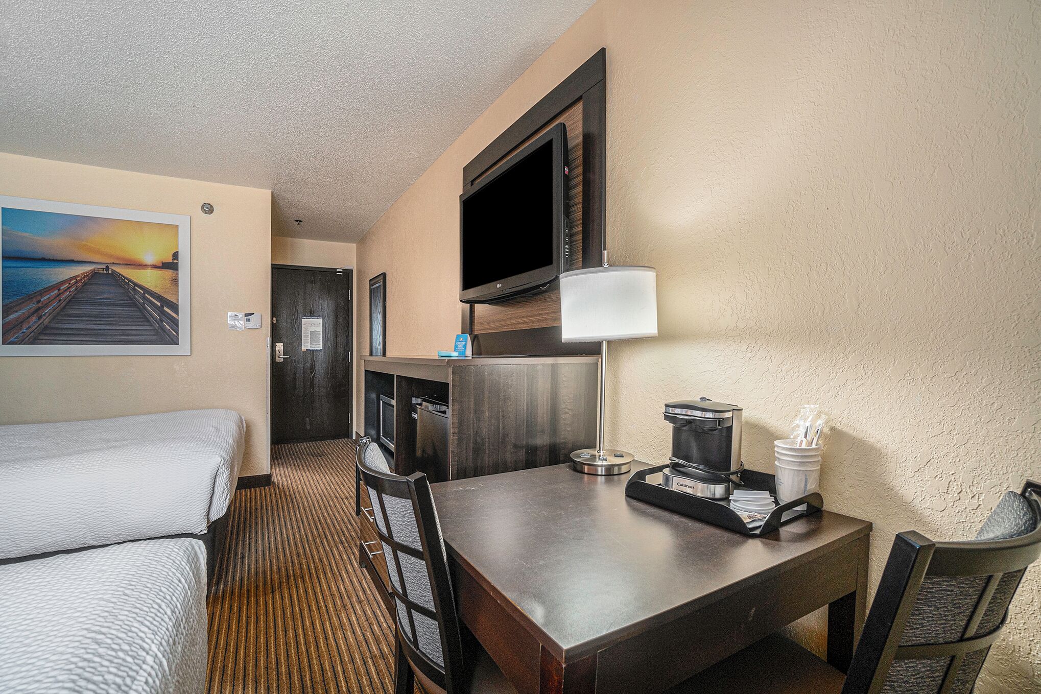 A hotel room with a bed, a desk, a chair, a TV, a lamp, and a coffee maker.