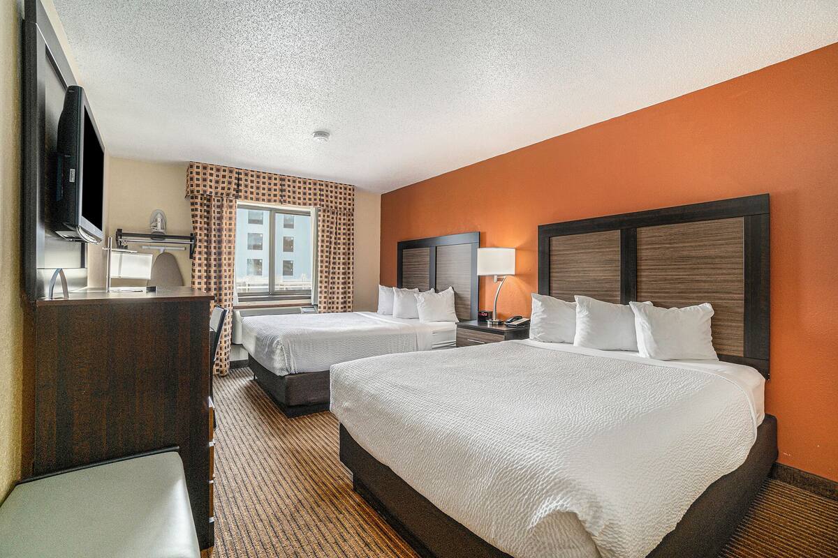A hotel room with two beds, a television, a desk, and a window with patterned curtains.