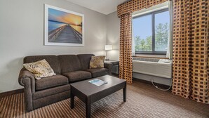 Une chambre d’hôtel avec un canapé, une table basse, une lampe et une grande fenêtre ornée de rideaux à motifs.