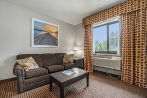 Habitación de hotel con sofá, una mesa de centro, una lámpara y un ventanal con cortinas estampadas.