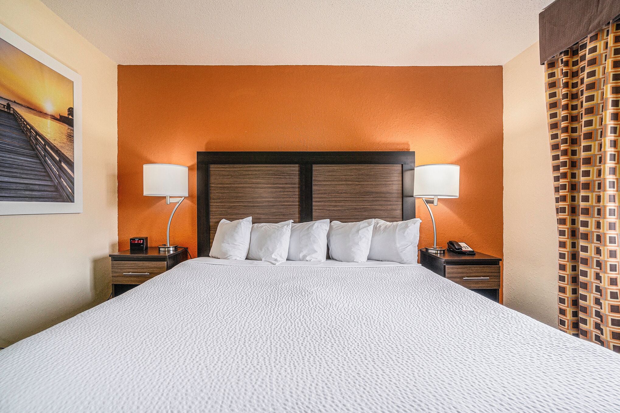 A hotel room with a large bed, two bedside tables with lamps, a nightstand with a phone, and a wall-mounted picture.