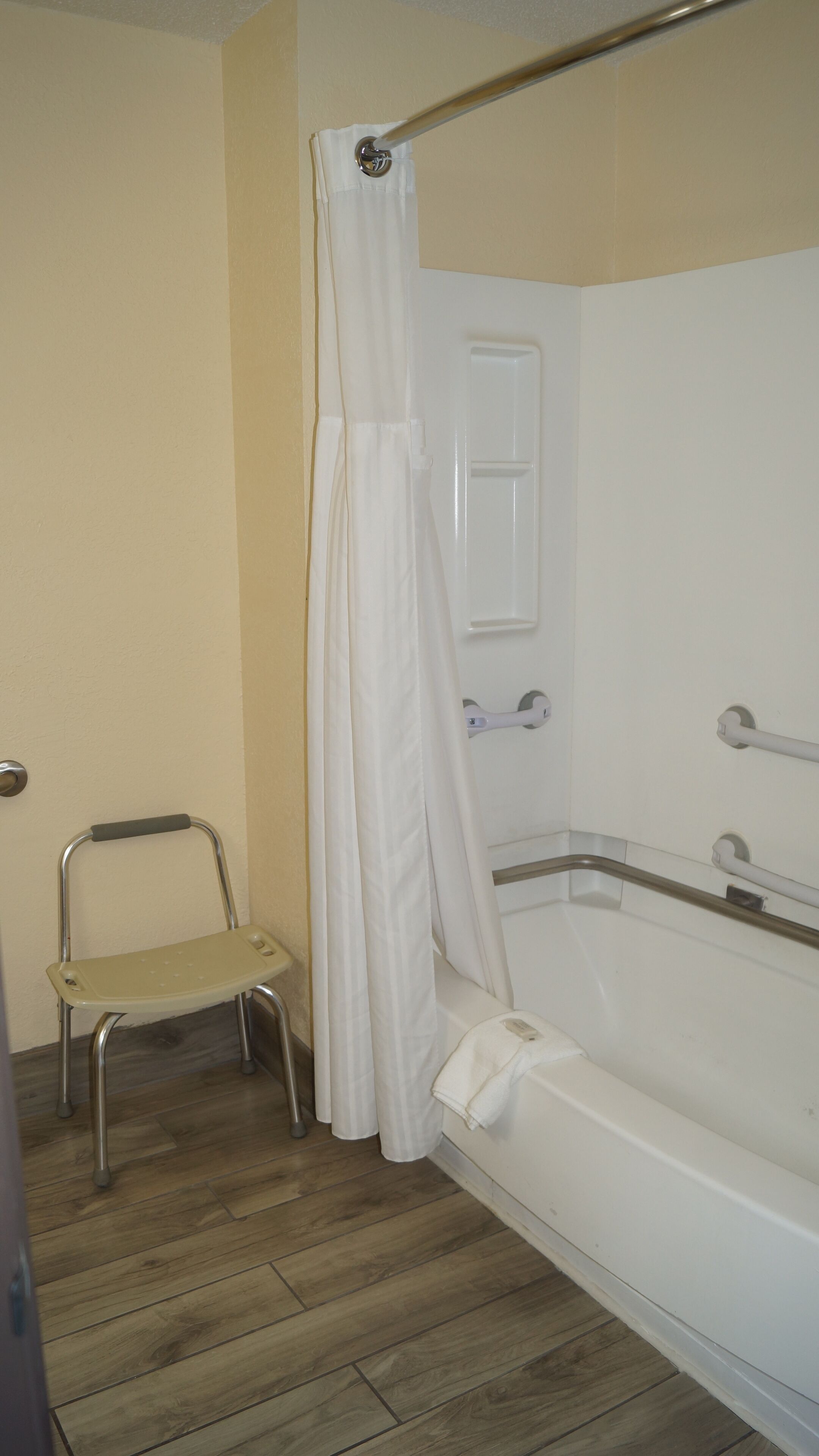 A bathroom with a bathtub, a shower curtain, a white door, and a small step stool.