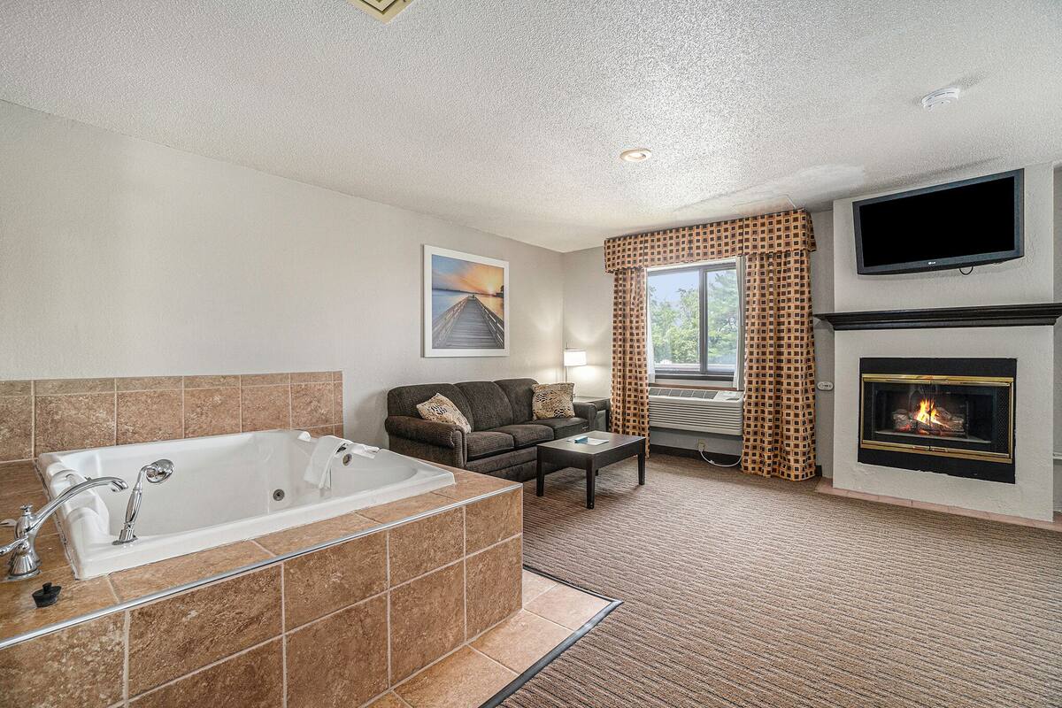 A modern bathroom with a large bathtub, a sofa, a flat-screen TV, and a fireplace.