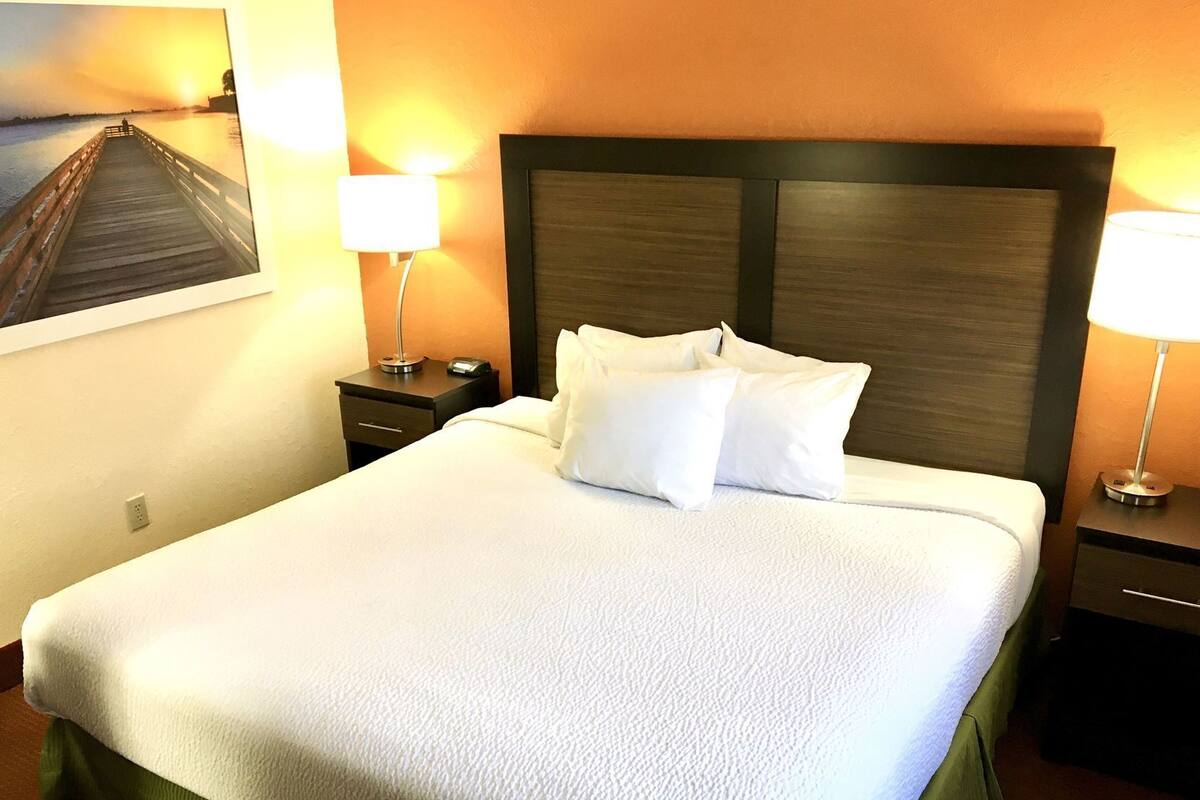 A neatly made bed with white bedding, a wooden headboard, and two bedside lamps.