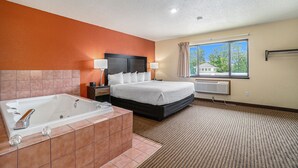 Une chambre d’hôtel avec un grand lit, une salle de bain séparée avec une baignoire, une fenêtre avec des rideaux et une vue sur des arbres et un immeuble.