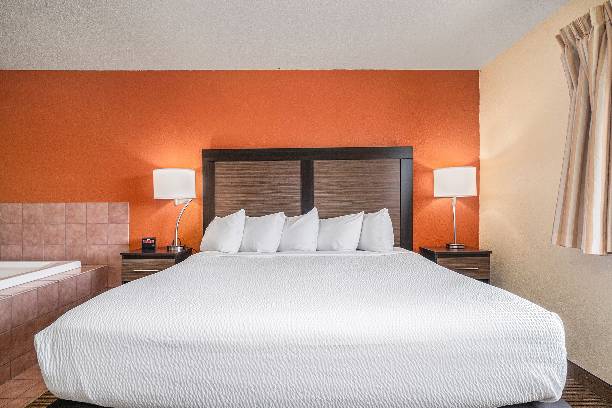 Une chambre d’hôtel avec un grand lit, deux tables de chevet avec des lampes, une tête de lit et une vue sur l’extérieur.