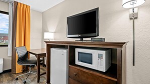 Habitación de hotel con televisor de pantalla plana, microondas, refrigerador, escritorio de madera, una silla y ventana con cortinas.