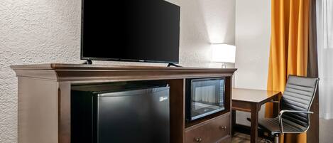Habitación de hotel con televisión de pantalla plana sobre un mueble, un escritorio con silla y una ventana con cortinas naranjas.