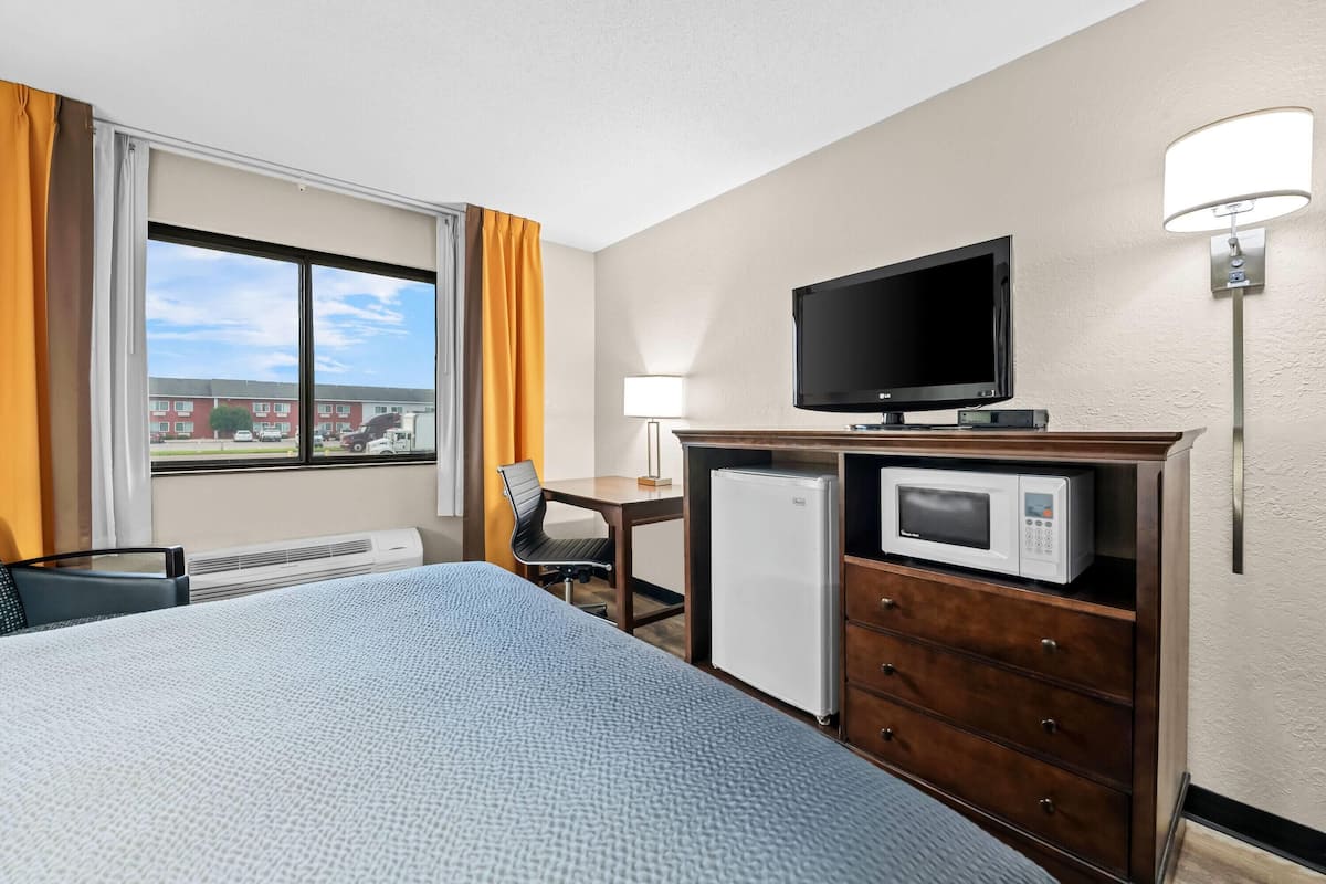 A hotel room with a bed, a desk, a television, a microwave, and a refrigerator.