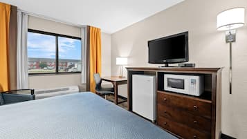 Habitación de hotel con cama, escritorio, televisor, microondas y refrigerador.