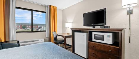 Habitación de hotel con cama, escritorio, televisor, microondas y refrigerador.
