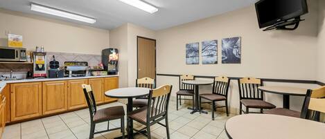 A clean, well-lit room with a kitchen area, seating for six, and a flat-screen TV mounted on the wall.