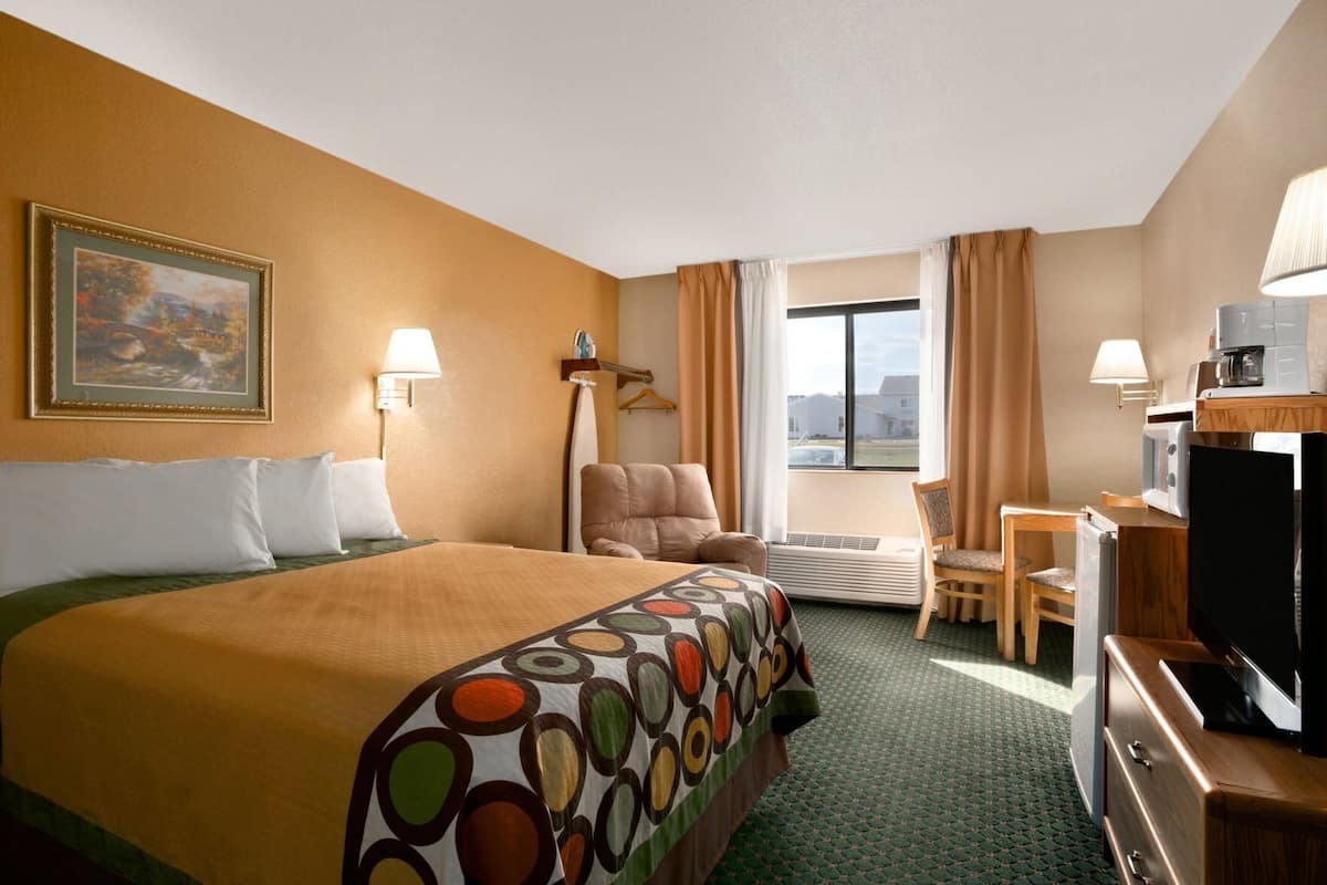 A hotel room with a bed, a desk, a chair, a television, and a window with curtains.