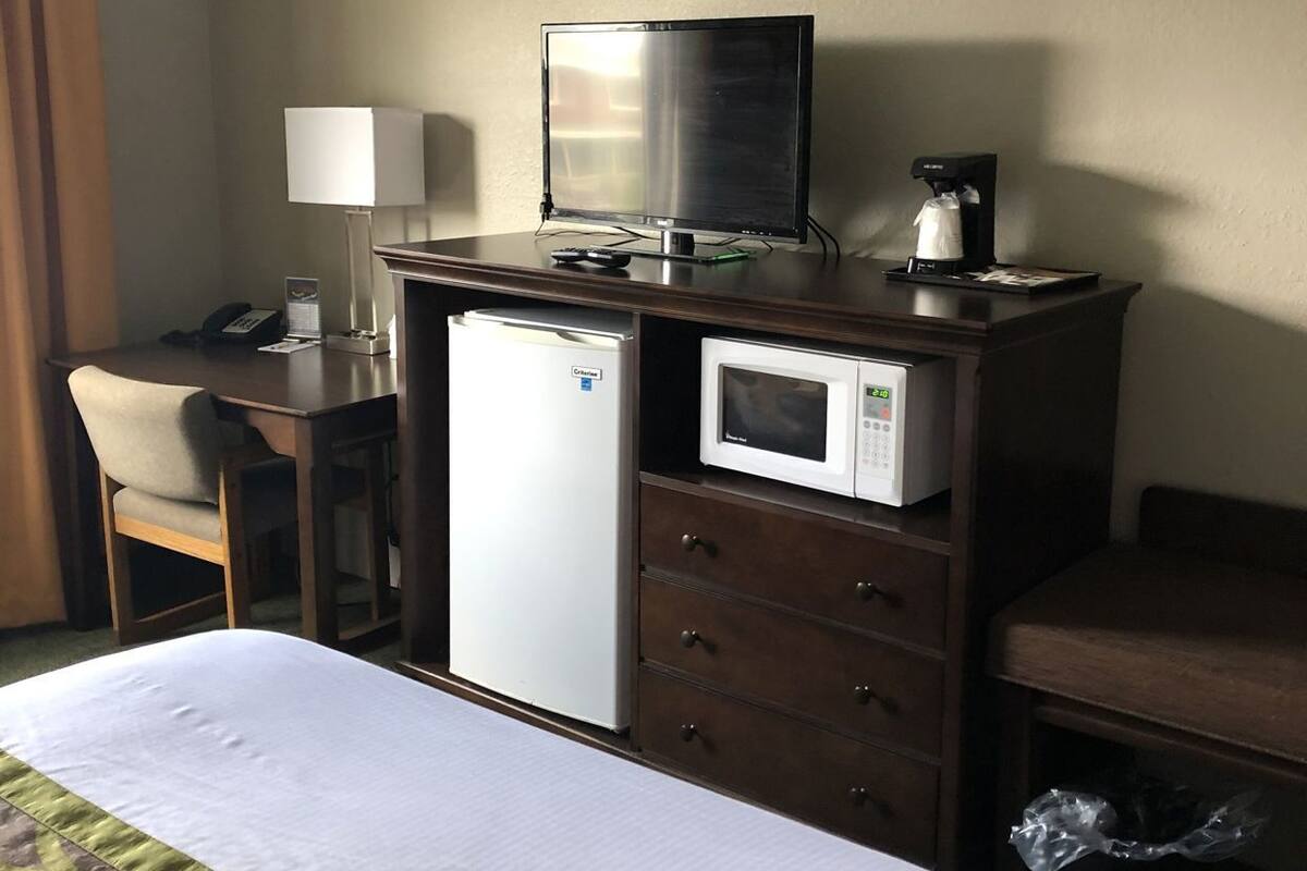 A hotel room with a bed, a desk with a computer, a microwave, and a coffee machine.