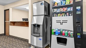 Máquina expendedora con aperitivos y bebidas, dispensador de agua y un estante pequeño con un ordenador portátil.