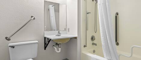 A bathroom with a toilet, sink, shower, and grab bars.