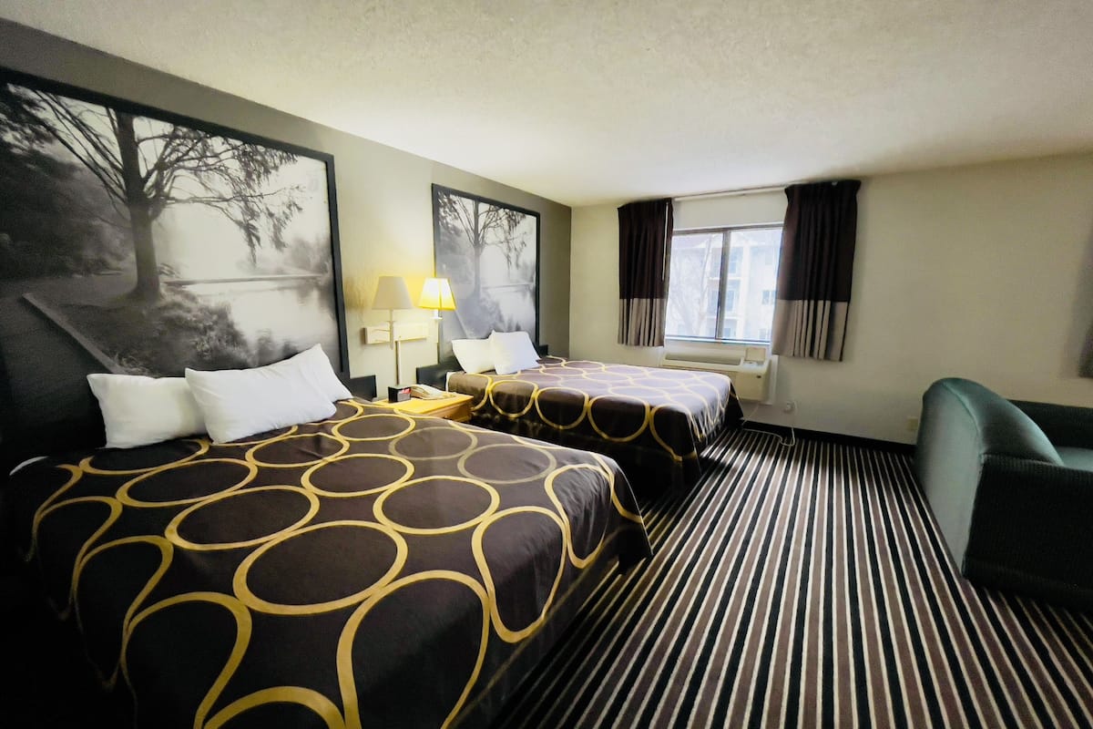 A hotel room with two beds, a desk, a chair, a window with curtains, and a wall with a painting.