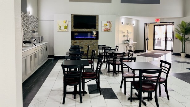 Un comedor moderno con una barra de cocina, varias mesas y sillas, un televisor de pantalla plana y una pared decorativa con obras de arte enmarcadas.