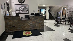 Zona de recepción con mostrador de piedra, un reloj y un cuadro enmarco. Una escalera conduce a otro nivel.