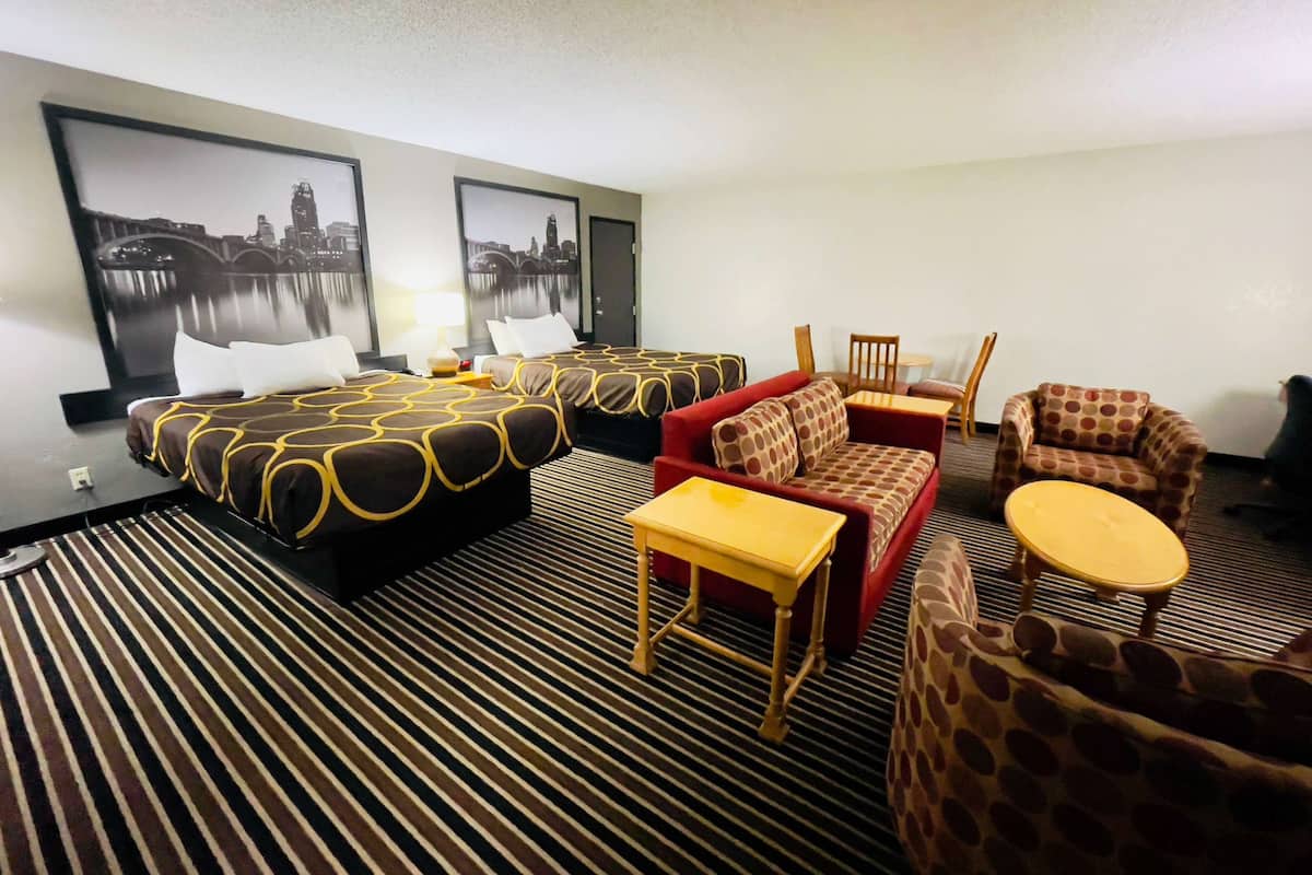 A hotel room with two beds, a red sofa, a small table, and a chair.