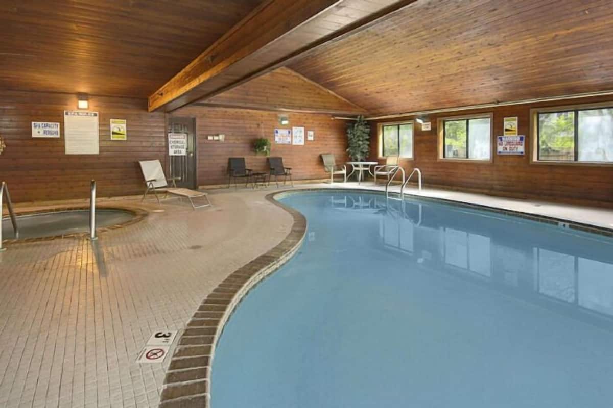 An indoor swimming pool with a wooden interior, lounge chairs, and a small hot tub.