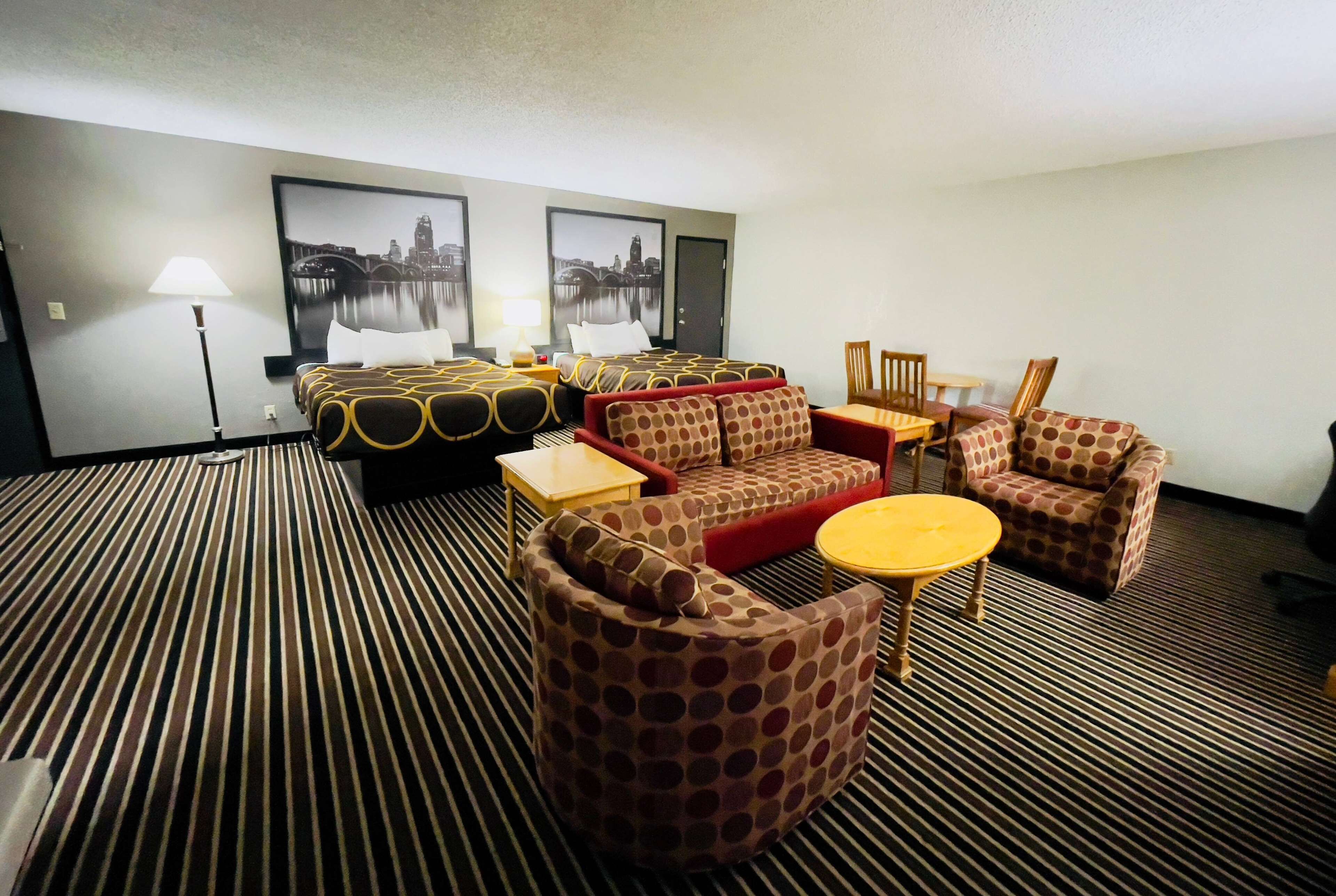 A hotel room with a striped carpet, a sofa set, a round table, and two framed pictures on the wall.